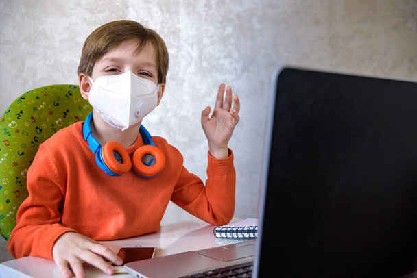 Coronavirus-Ausbruch. Sperrung und Schulschließungen. Schuljunge mit Gesichtsmaske beobachtet Online-Bildungskurse und fühlt sich zu Hause gelangweilt und deprimiert. COVID-19-Pandemie zwingt Kinder zum Online-Lernen. - Foto, Bild