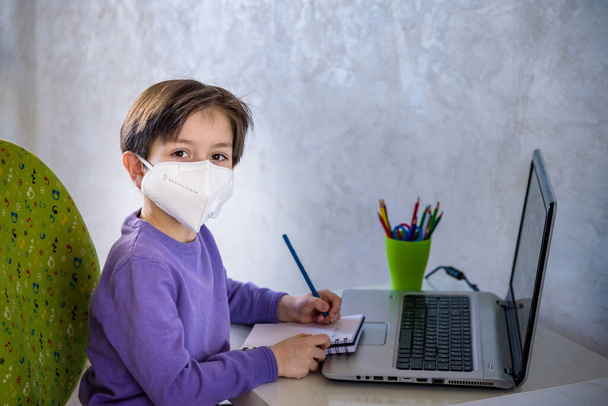 boy with computer does his homework during a coronavirus quarantine. concept of online education. Social distance, self- isolation. Distance learning due to virus, infection, and flu epidemic COVID-19 - Photo, Image