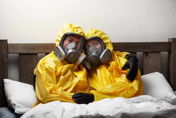 zwei Personen, die sich im Bett isolieren, sind besonders vorsichtig und tragen Schutzanzüge - Foto, Bild