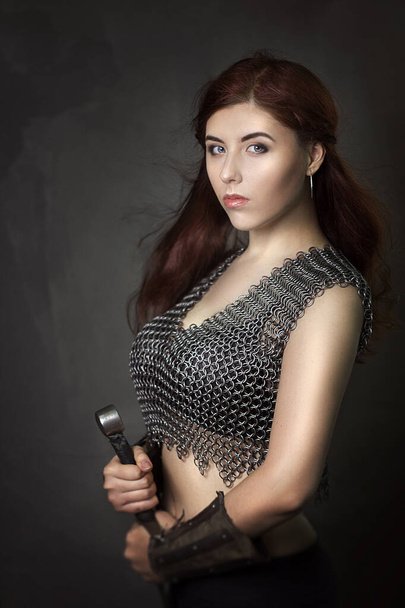 Beautiful girl warrior in chain mail with a sword in his hands. Medieval fantasy valkyrie with long hair posing on a dark background. - 写真・画像