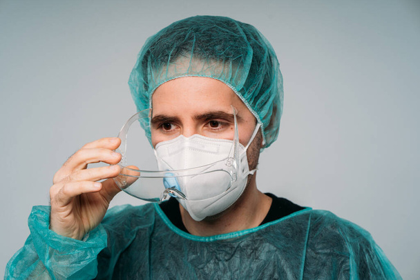 COVID-19 Koronavirová pandemie, muž lékař nasadit brýle, lékařská maska, brýle, latexové rukavice a ochranné oděvy proti viru - Fotografie, Obrázek