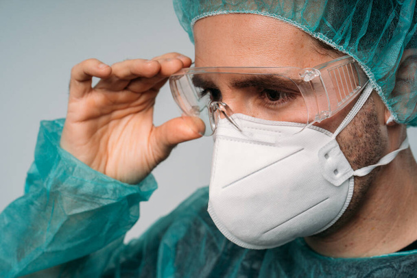 COVID-19コロナウイルスのパンデミック、眼鏡、医療用マスク、眼鏡、ラテックス手袋、ウイルスに対する保護服を身に着けている男性医師 - 写真・画像
