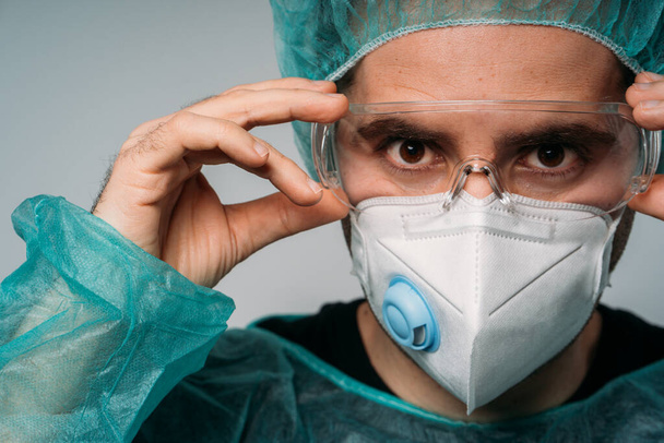 COVID-19コロナウイルスのパンデミック、眼鏡、医療用マスク、眼鏡、ラテックス手袋、ウイルスに対する保護服を身に着けている男性医師 - 写真・画像