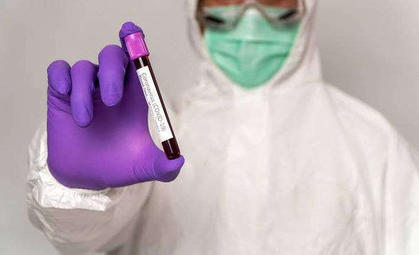 Doctors in the protective suits and masks are holding a positive blood test result for new rapidly outbreaking Coronavirus. Concept of spreading Coronavirus (COVID-19) around the world, USA, Europe - Photo, Image
