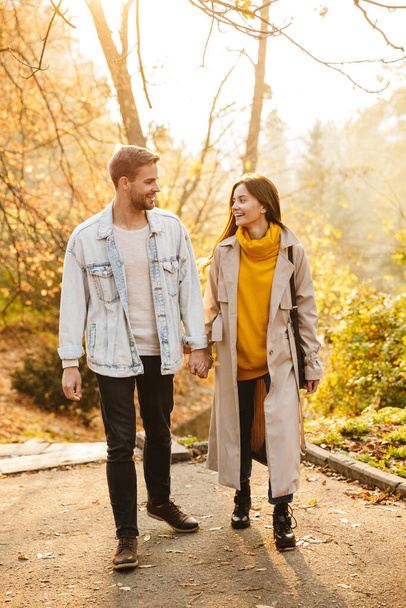 Immagine di attraente giovane coppia caucasica sorridente e passeggiando nel parco autunnale insieme
 - Foto, immagini