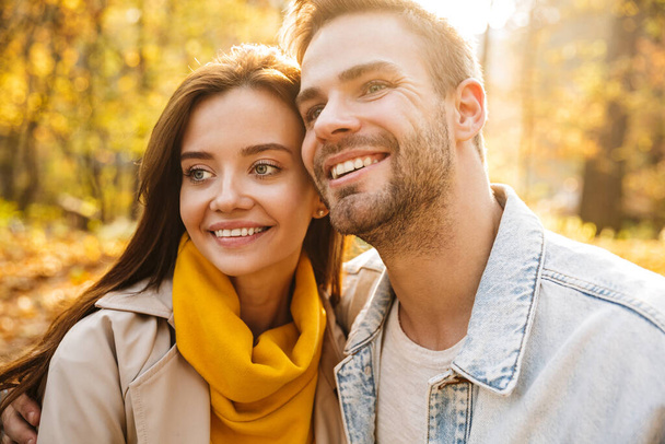 Image of attractive young caucasian couple smiling and walking through autumn park together - Zdjęcie, obraz