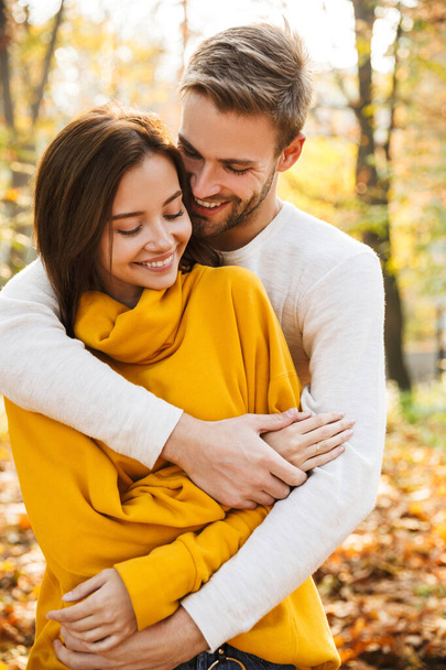 Image of attractive young caucasian couple in love hugging while walking at autumn park - Fotoğraf, Görsel