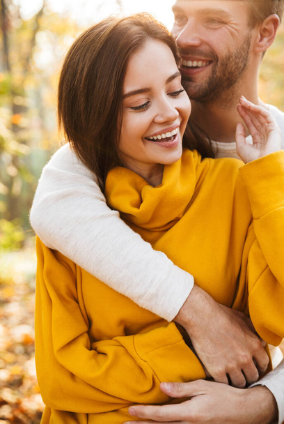Image of attractive young caucasian couple in love hugging while walking at autumn park - Photo, Image
