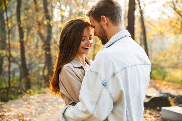 Image of attractive young caucasian couple smiling and walking through autumn park together - Zdjęcie, obraz