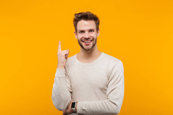 Attractive happy young man wearing pullower standing isolated over yellow background, presenting copy space - Zdjęcie, obraz