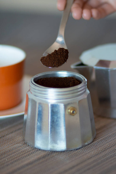 Рука держит ложку с молотым кофе, прежде чем наливать его в кофеварку
 - Фото, изображение