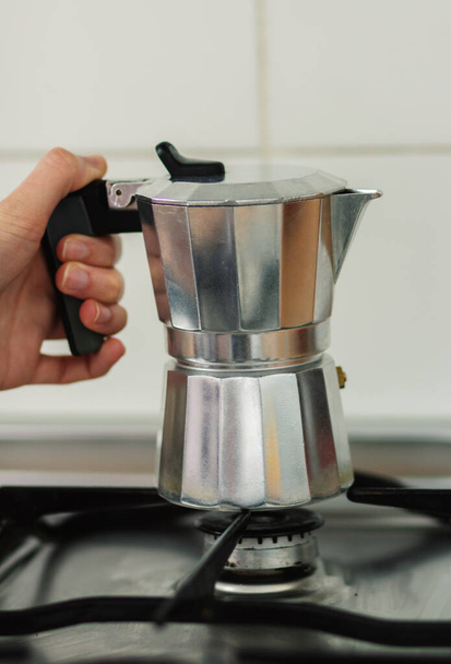 Een hand houdt een koffiepot op het fornuis - Foto, afbeelding