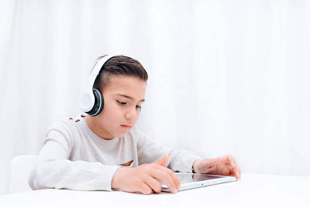  Bambino studio online seduto con tablet e cuffie. Bambino che ascolta l'insegnante e guarda su tablet
 - Foto, immagini