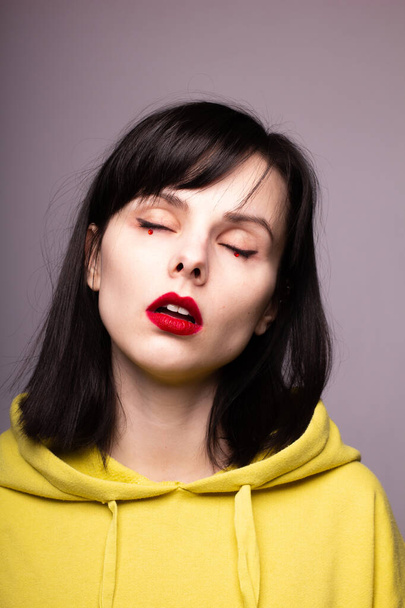 woman in a hoodie with red lipstick on the lips and dots under the eyes - Фото, зображення