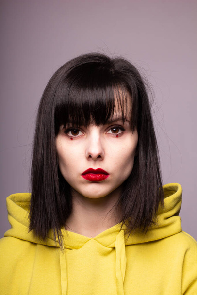 woman in a hoodie with red lipstick on the lips and dots under the eyes - Foto, afbeelding