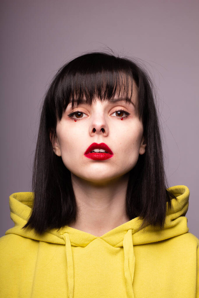 woman in a hoodie with red lipstick on the lips and dots under the eyes - Foto, Imagen