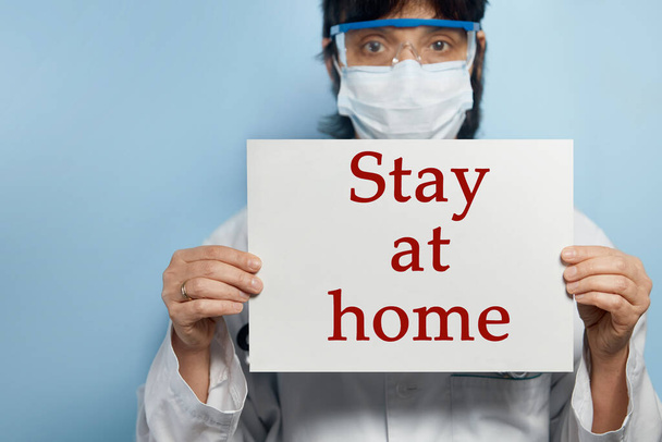 A doctor with a paper with text STAY AT HOME holding on hand, protect from Coronavirus or Covid-19 epidemic - 写真・画像