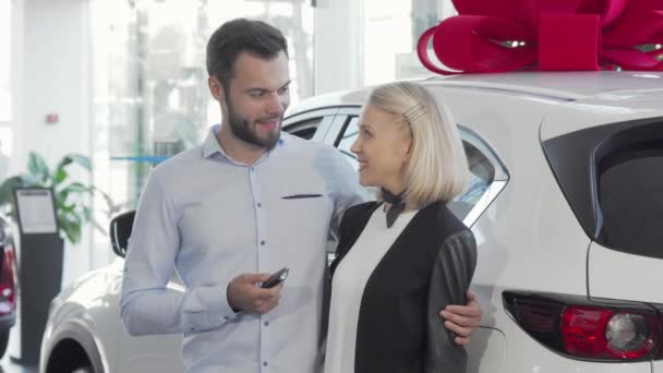 Ευτυχισμένο νεαρό ζευγάρι στέκεται κοντά στο νέο τους αυτοκίνητο στην αντιπροσωπεία - Πλάνα, βίντεο