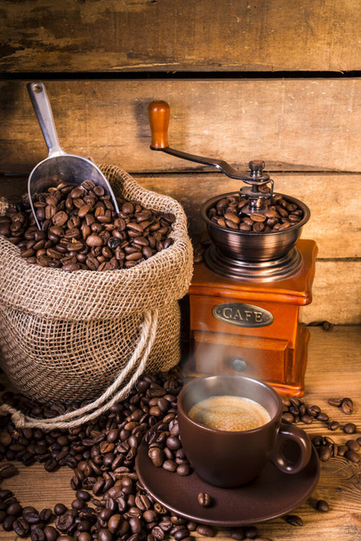 кавові зерна в джутовому мішку з дерев'яною шліфувальною машиною і чашкою кави на пару
 - Фото, зображення
