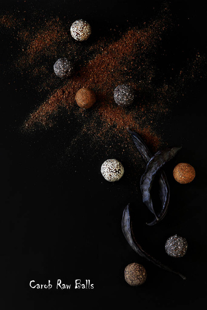 Homemade carob, fig and almond raw balls, carob powder end carob fruit on black background. Vegetarian dessert.  Healthy food. Concept promotional flyer and poster. Flat lay - Photo, Image