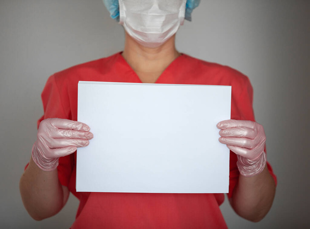 Women doctor wearing gloves and protective mask, holding empty paper. - Foto, Bild