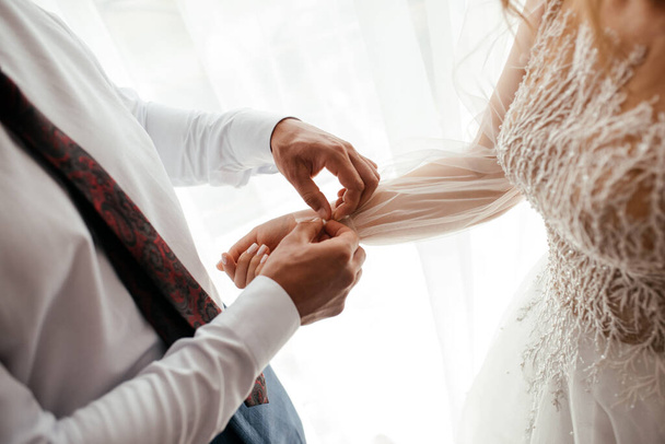 Bruidegom helpt een bruid met haar jurk, romantisch concept - Foto, afbeelding