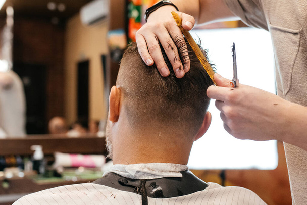 Cropped view of hairdresser doing hairstyle and style with scissors and comb. Concept Barbershop. - Photo, Image