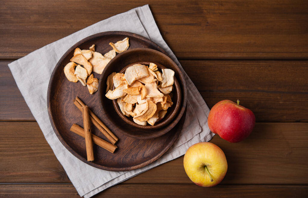 dolci chips di mele fatte in casa essiccate con cannella in ciotola di legno su sfondo di legno. Prodotto vegano e dietetico. Vista dall'alto e spazio di copia
 - Foto, immagini