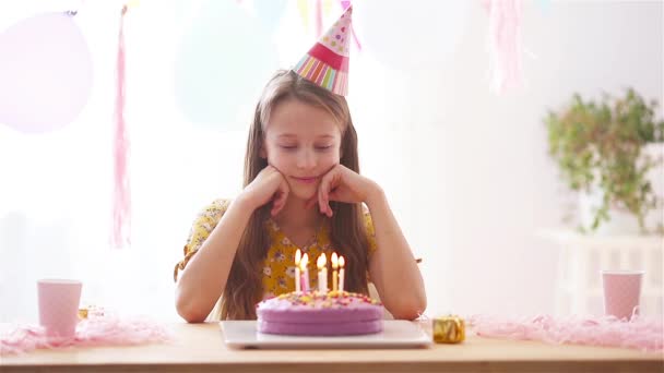 白人の女の子は夢のように笑って誕生日の虹のケーキを見ています。風船で祭りのカラフルな背景。誕生会と願いのコンセプト. - 映像、動画