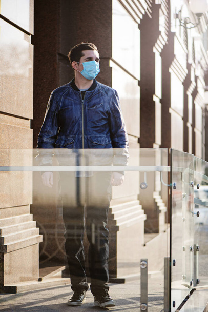Modern bir binanın arka planında koruyucu maskeli genç bir adamın portresi. - Fotoğraf, Görsel