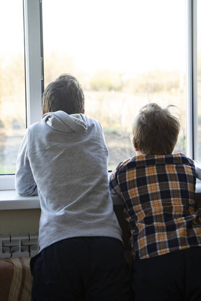 Two boy look in window in Pandemic isolation - Child sitting on windowsill during coronovirus, covid-19. - Photo, Image