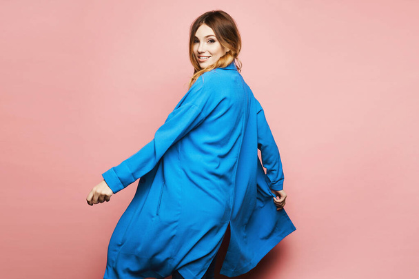 Young happy woman in a blue coat spin around on the pink background. Copy space for advertising. Sale. Discount - Photo, image