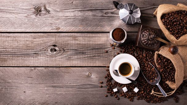 Auf dem rustikalen Holztisch eine Tasse heißen Kaffee, eine Kaffeemühle, einen italienischen Mokka und Kaffeebohnen. Blick aus dem Hochwinkel - Foto, Bild