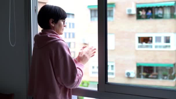 Vrouw van middelbare leeftijd klapt in het raam ter ondersteuning van mensen die vechten tegen het coronavirus - Video