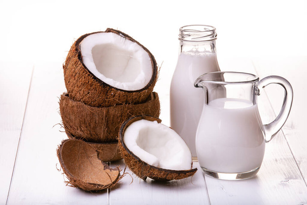 na bílém stole, karafě a láhvi s kokosovým mlékem, části naskládaných kokosů - Fotografie, Obrázek