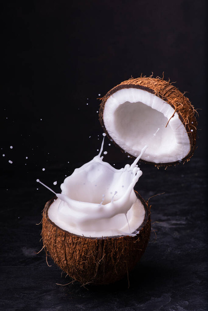 Zwei Hälften einer Kokosnuss und Spritzer Kokosmilch vor dunklem Hintergrund - Foto, Bild