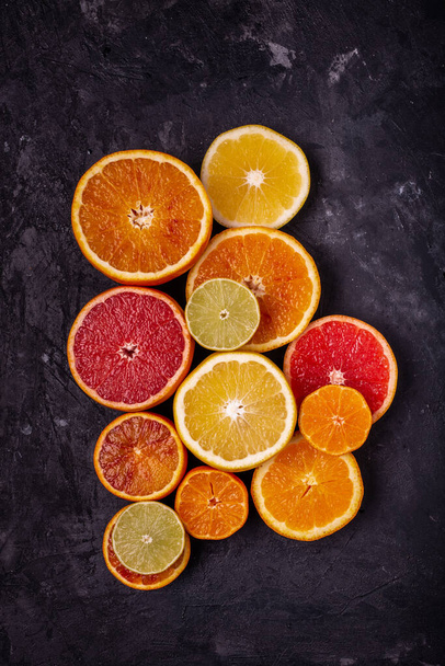 top view of various types of citrus fruits, cut into slices and laid on a rustic background, black - Fotó, kép