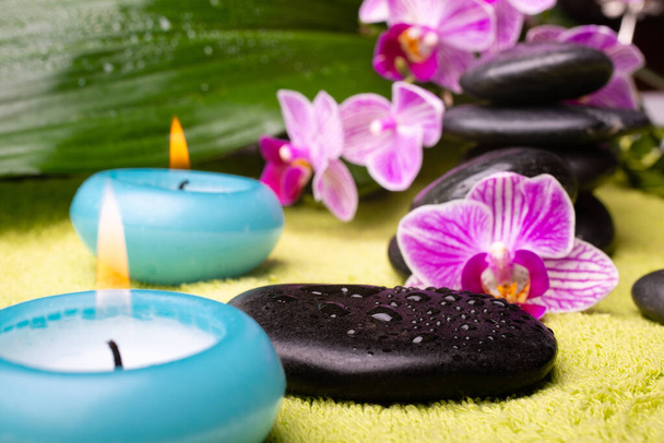 spa concept. a lit candle in the foreground, and stones with orchids in the background - Photo, Image