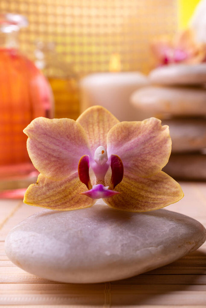 Centro benessere. In primo piano un'orchidea. Sullo sfondo candele, pietre impilate e bottiglie con essenze profumate
 - Foto, immagini