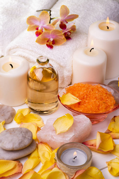 Wellness center. Composition with orange-flavored bath salts, transparent glass bottle with perfumed essential oil, white towels, rose petals and candle. - Photo, Image