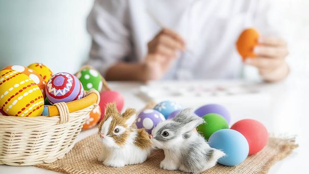 Oeufs de Pâques et décoration sur un bureau blanc avec une femme heureuse peignant fond d'œufs. La famille se prépare pour Pâques. - Photo, image