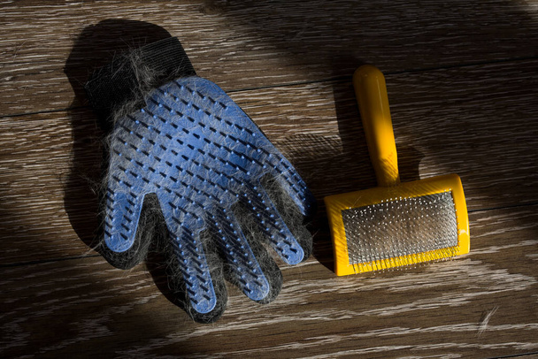Blue glove and a yellow comb with cat or dog hair on the hardwood floor for combing animals. - Photo, Image