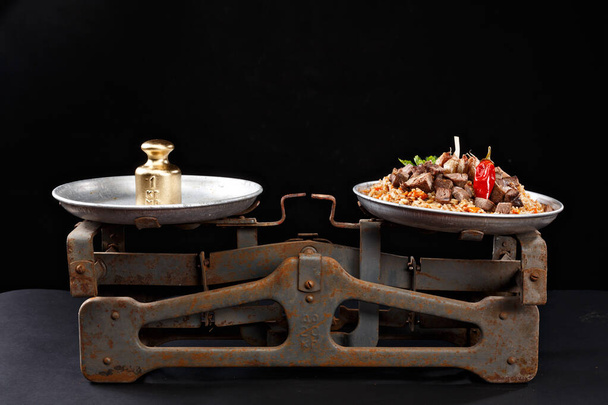 Concept photo. PILAF is equal to gold. Plov like value. Food and gold in rusty weights.  - Valokuva, kuva