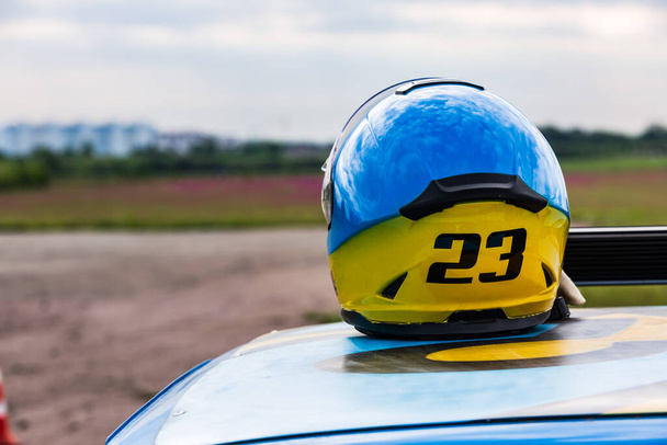 Casco autosport amarillo-azul con el número 23 en el techo azul del coche en el fondo de un campo de flores
 - Foto, Imagen