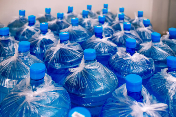 Een rij grote flessen drinkwater voor een koeler. Watervoorziening. Verpakt en klaar om te worden verzonden naar klanten, blauwe flessen, afgewerkte goederen magazijn, schoon water - Foto, afbeelding
