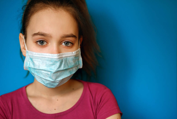 Een meisje met een beschermend medisch masker tegen een virus op een blauwe achtergrond, pandemie, coronovirus infectie, Covid-19, de wereldwijde epidemie, bescherming tegen coronovirus, luchtinfectie - Foto, afbeelding