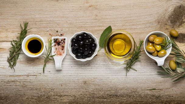 top view, on the rustic wooden table, the arrangement of bowls with olives, variety of spices, olive branch and extra virgin olive oil. Still life - Photo, image