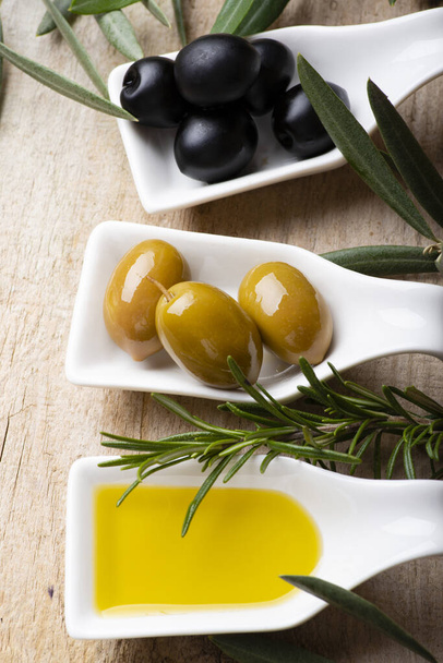 in the foreground, on the rustic wooden table, some white ceramic bowls with green and black olives and extra virgin olive oil. - Photo, image