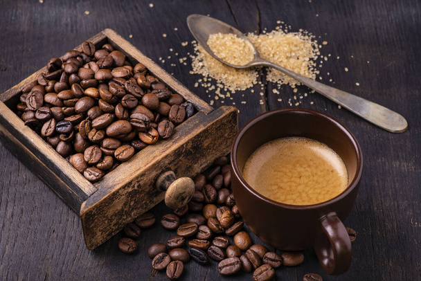 Sur la table en bois brut et sombre, une tasse de café avec une cuillerée de sucre brun et des grains de café torréfiés
. - Photo, image