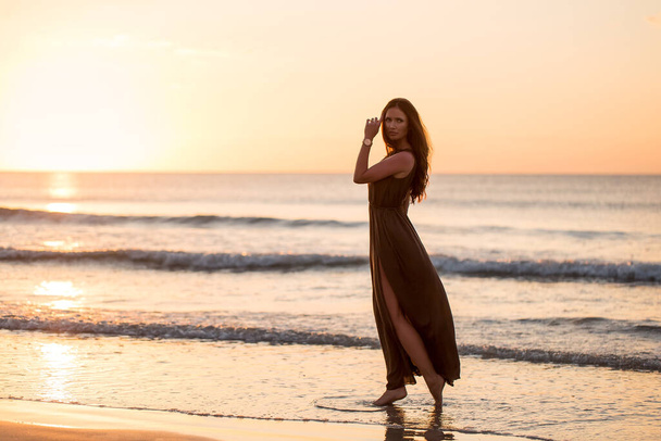 Beautiful woman on sunset background. Colorful dawn over the sea. Carefree woman enjoying the sunset on the beach. Happy lifestyle. - Фото, зображення
